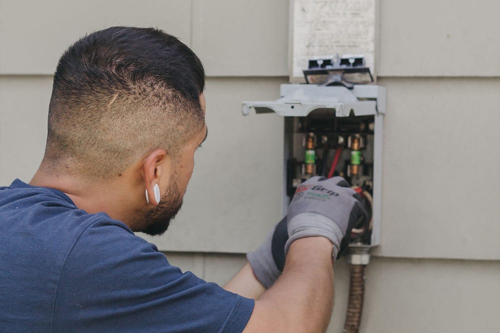 Licensed HVAC technician repairing AC electrical panel outside home
