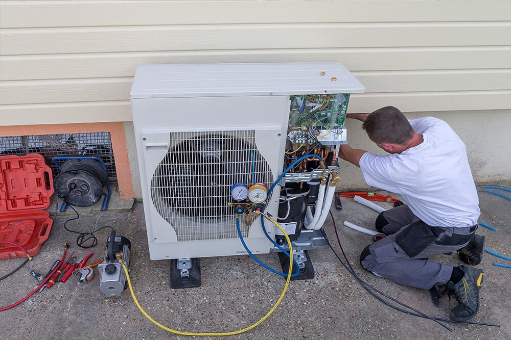 man in white short checking wiring of heat pump