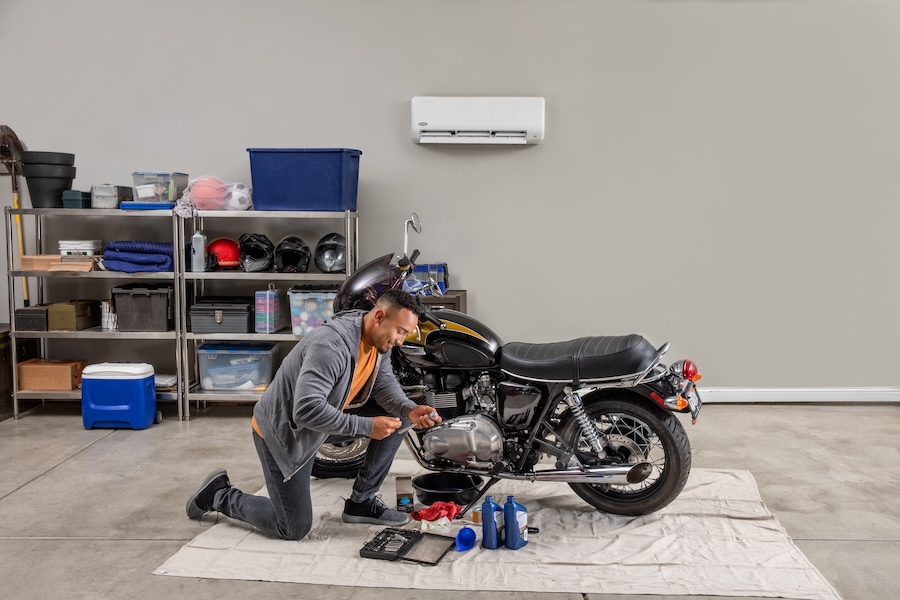 man working on motorcycle in his garage with his newly installed ductless sytem.