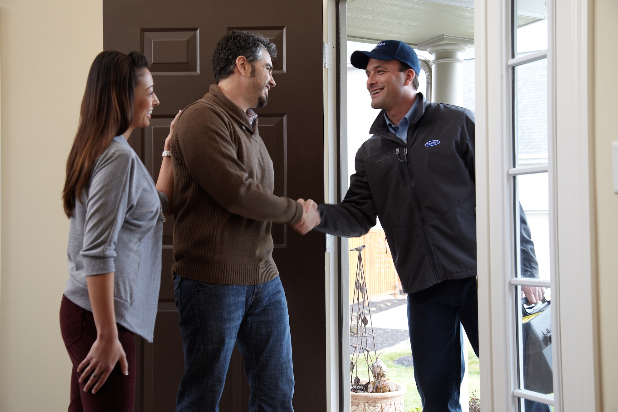 Service tech coming to install humidifier greeting couple at front door.